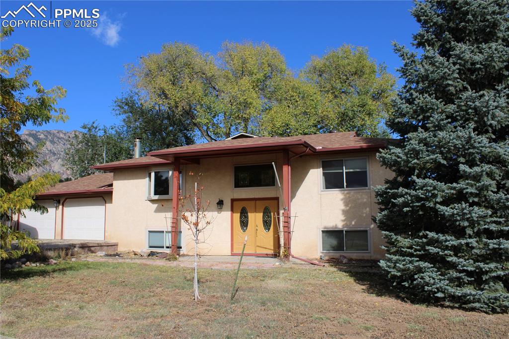 Caption: View of front of house with stucco siding, a front yard, a garage, and a shingled roof