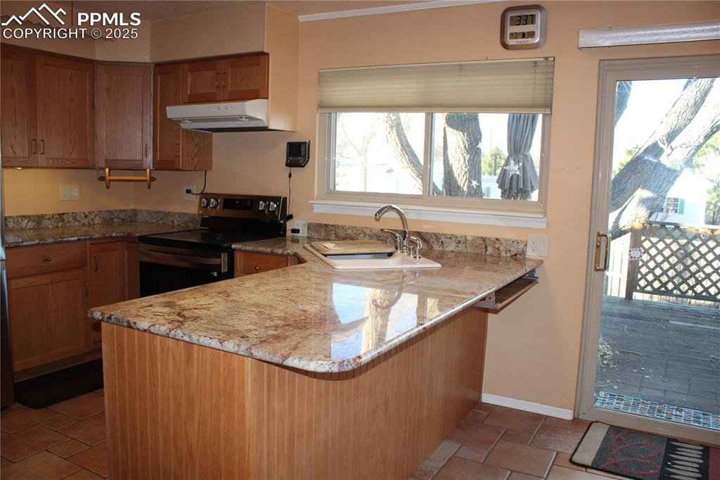 Image 18 of 48: Kitchen featuring a peninsula, brown cabinetry, electric stove, and light s