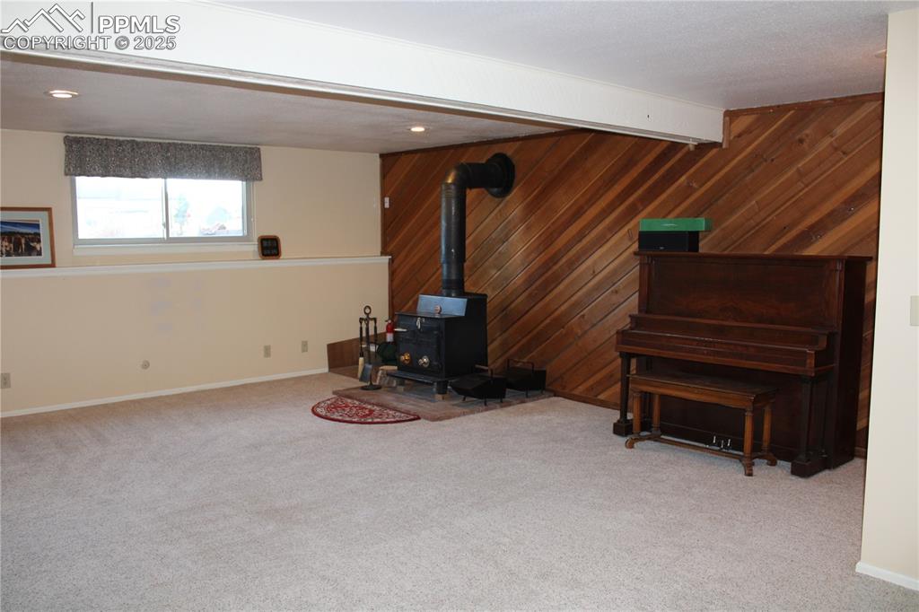 Image 38 of 48: Living area featuring a wood stove, wooden walls, and light carpet