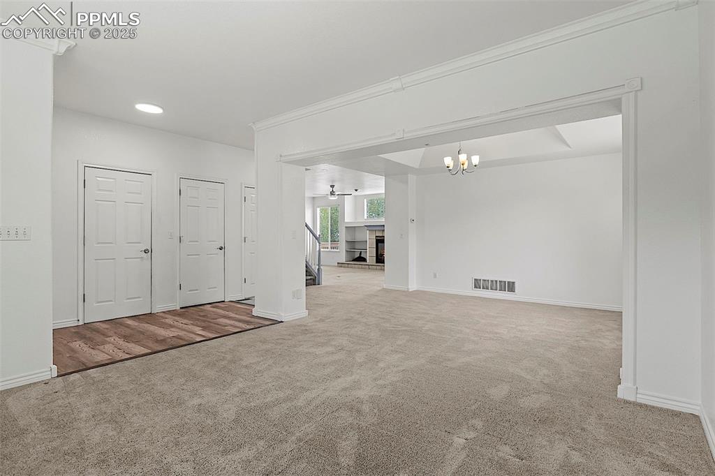 Image 10 of 48: Unfurnished room with carpet floors, a chandelier, baseboards, and a firepl