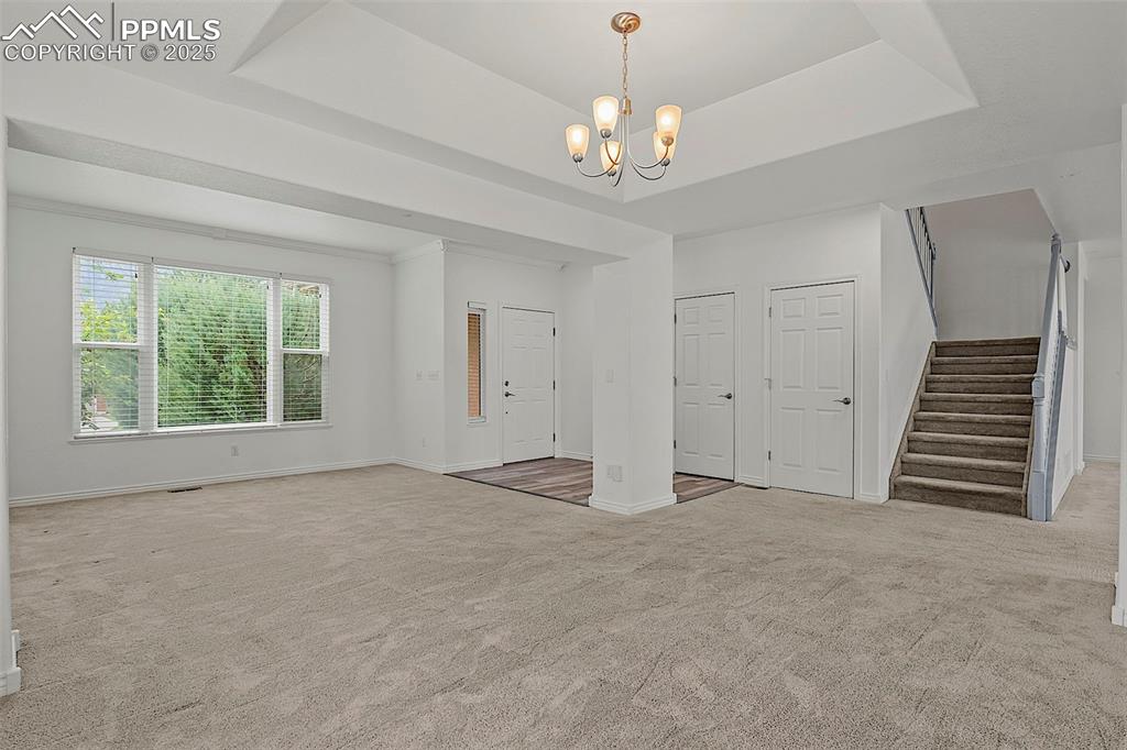 Image 11 of 48: Unfurnished living room featuring stairs, a chandelier, carpet floors, base