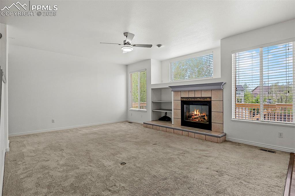 Image 12 of 48: Unfurnished living room with a ceiling fan, a tiled fireplace, baseboards, 