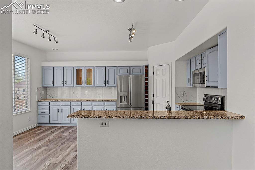 Image 17 of 48: Kitchen with stainless steel appliances, rail lighting, a peninsula, stone 