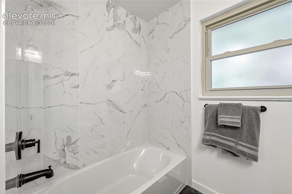 Image 14 of 30: Bathtub and shower surround featuring large format marble-look tile