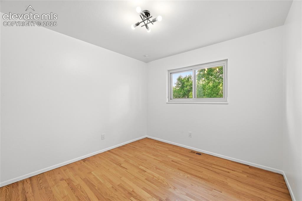 Image 15 of 30: Bright room featuring wood-finish flooring, white walls, and a contemporary