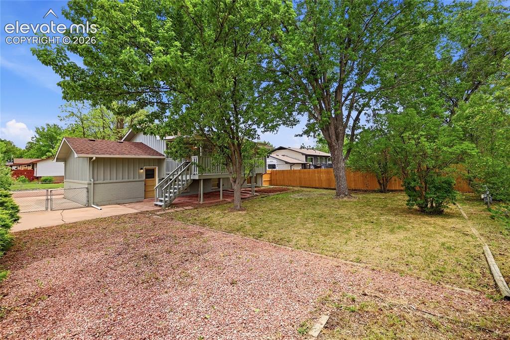 Image 25 of 30: Split-level residence featuring a gravel driveway, mature trees, and a wood