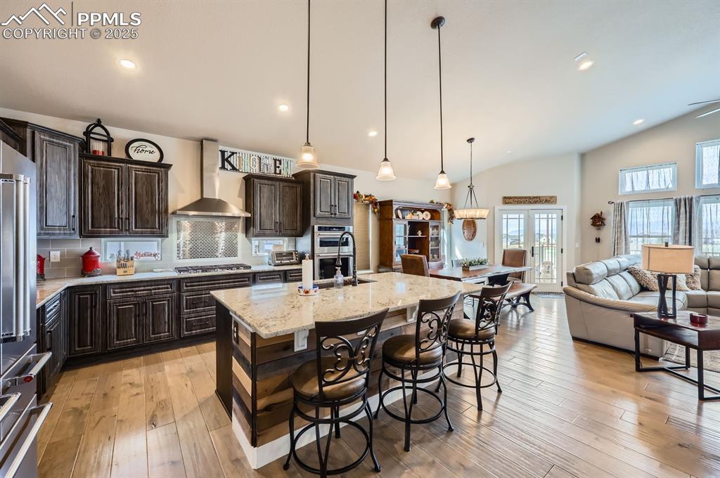 Image 6 of 27: Kitchen with wall chimney exhaust hood, lofted ceiling, appliances with sta