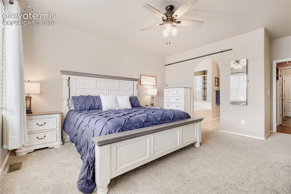 Image 11 of 31: Primary main level bedroom with a ceiling fan light fixture, large window w