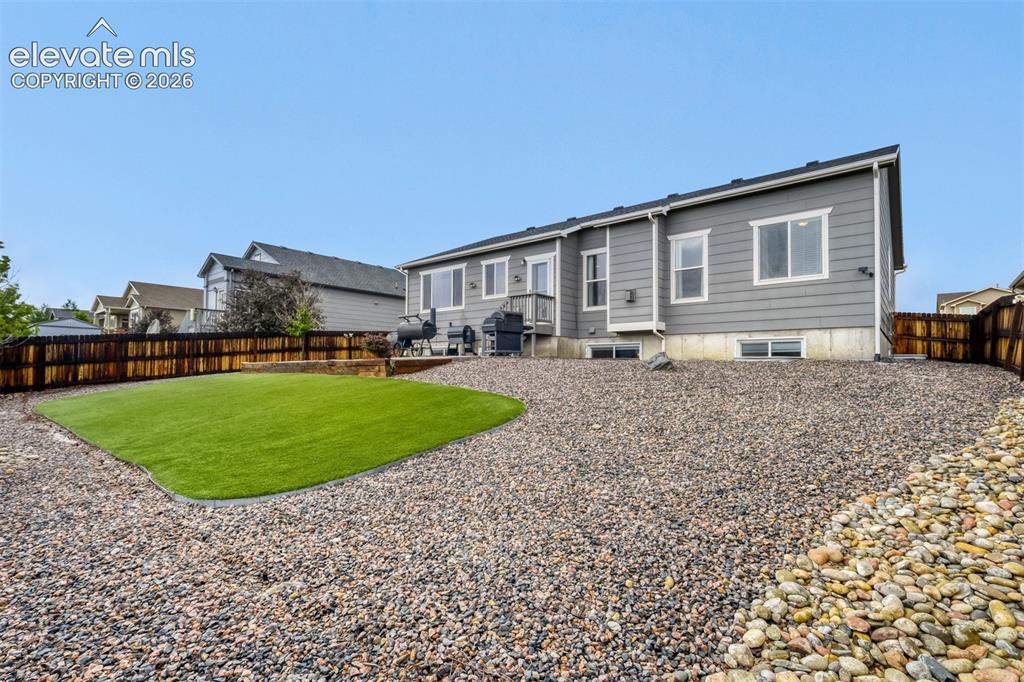 Image 28 of 31: Expansive backyard featuring a concrete patio, decorative gravel, and a woo