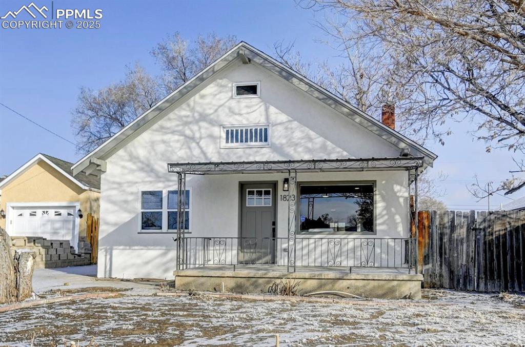Caption: View of front of home featuring covered porch, a chimney, fence, and stucco siding