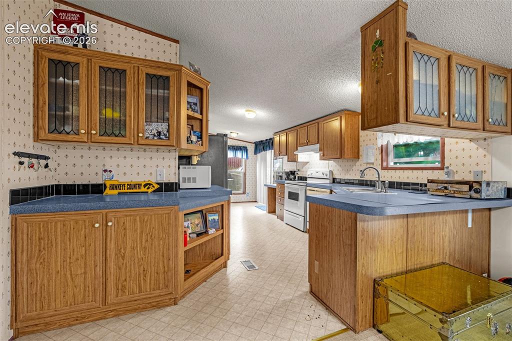 Image 7 of 38: Kitchen featuring wood-finish cabinetry with glass-front uppers, blue count