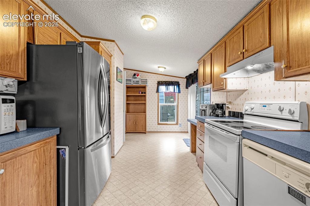Image 8 of 38: Kitchen featuring wood cabinetry, blue countertops, and white appliances in