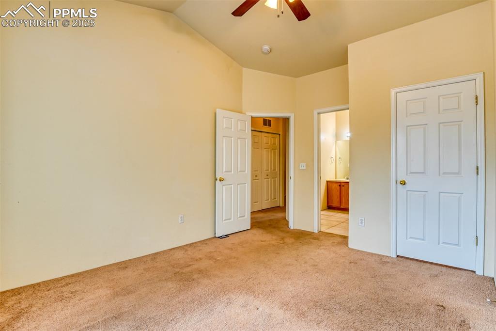 Image 28 of 32: Unfurnished bedroom with light colored carpet, vaulted ceiling, connected b