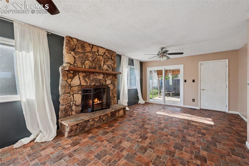 Image 12 of 41: Unfurnished living room with ceiling fan, a stone fireplace, stone finish f