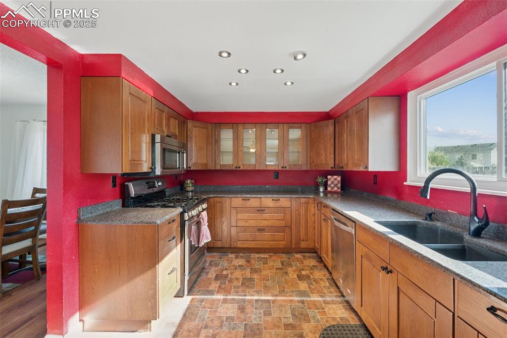 Image 16 of 41: Kitchen with stainless steel appliances, brown cabinetry, dark stone counte
