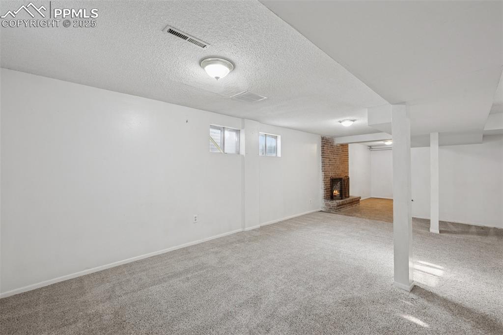 Image 28 of 41: Below grade area featuring carpet, a brick fireplace, and a textured ceilin