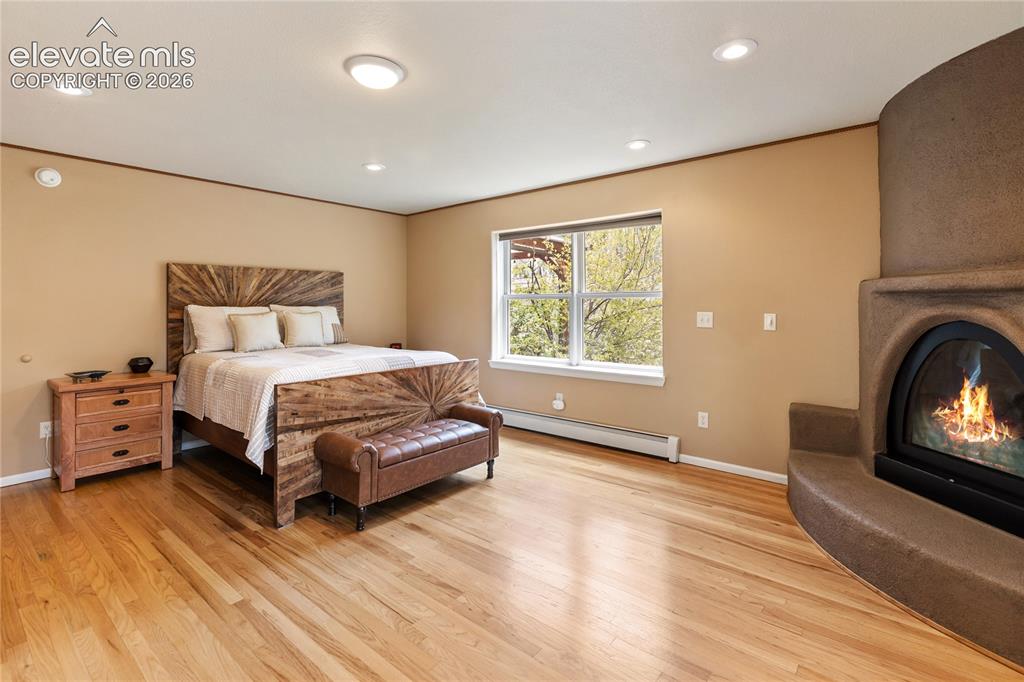 Image 15 of 40: Spacious primary suite with hardwood floors, a kiva-style fireplace, and ov