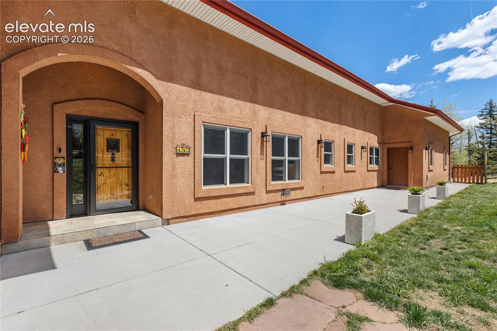Image 3 of 40: Stucco exterior with an arched entry, a natural wood front door, and a conc