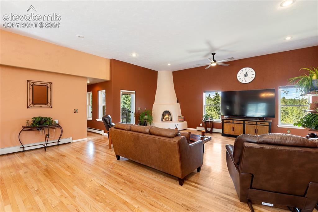 Image 4 of 40: Spacious living room with hardwood floors and a striking kiva-style firepla