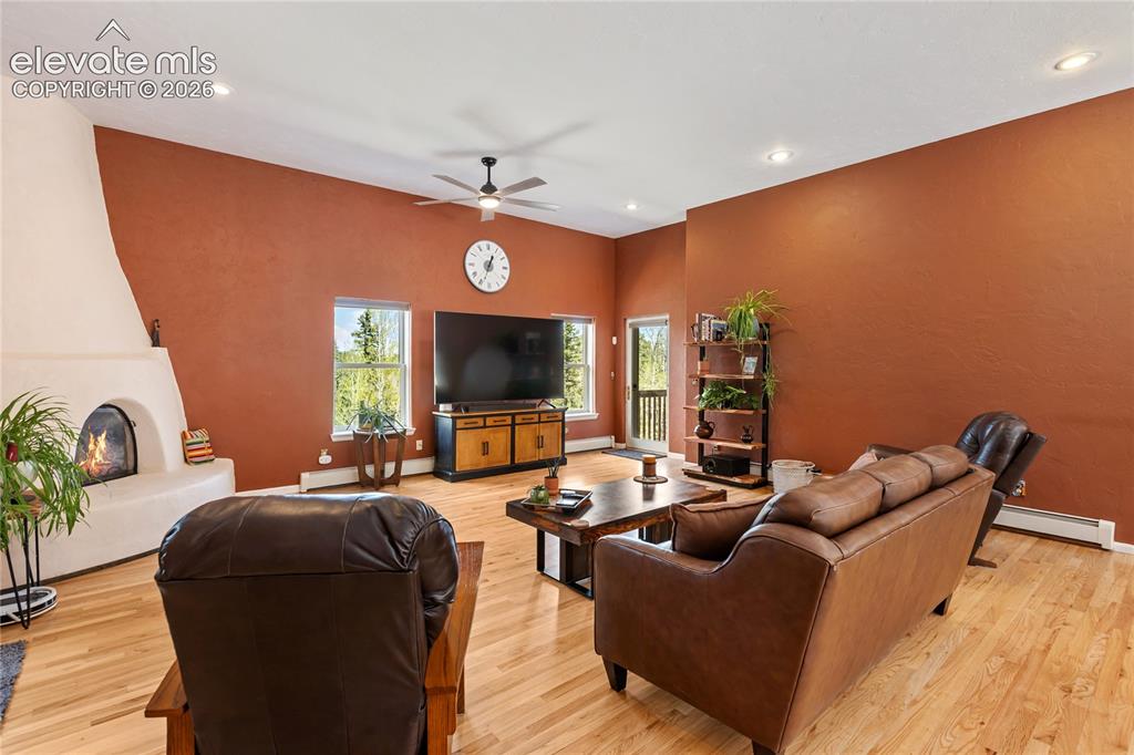 Image 5 of 40: Spacious living area featuring a kiva fireplace, wood-finish flooring, vaul