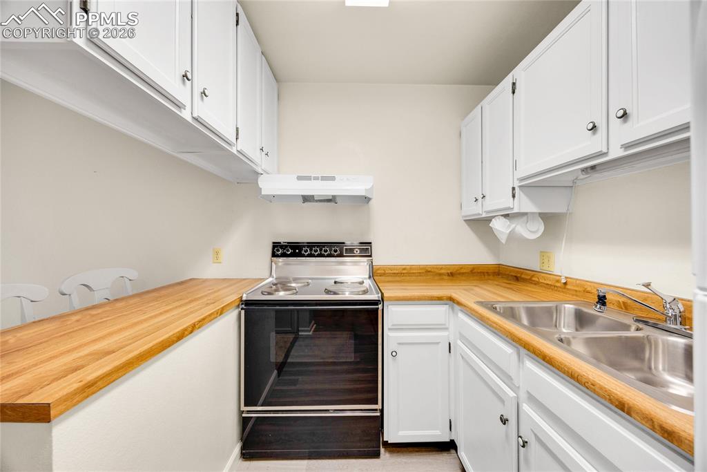 Image 5 of 17: Kitchen with electric range oven, white cabinetry, and under cabinet range