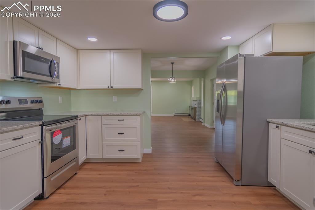 Image 9 of 18: Kitchen with stainless steel appliances, white cabinets, light wood-type fl