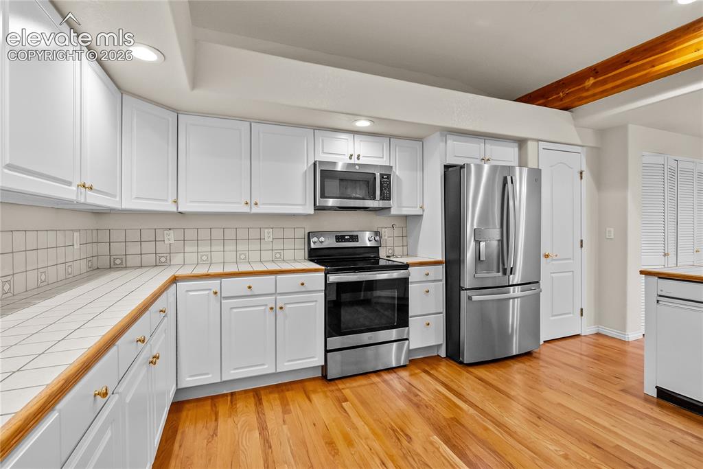 Image 11 of 41: Kitchen featuring white cabinetry, wood-finish countertops, tile backsplash