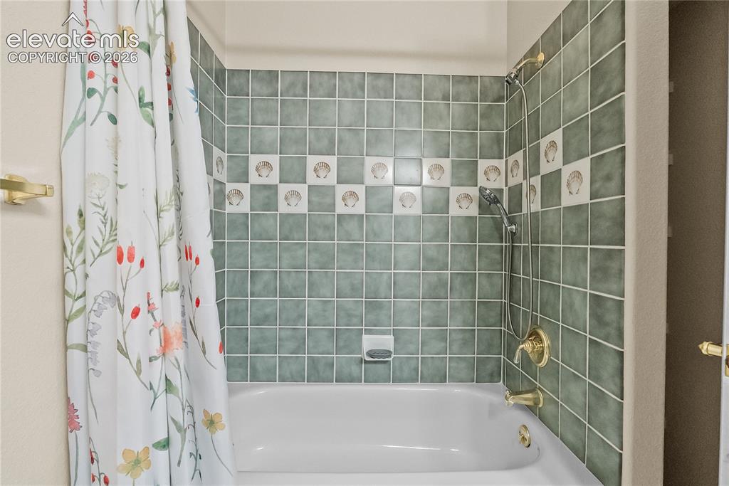 Image 22 of 41: White bathtub with brass fixtures, green tiled surround, and decorative she