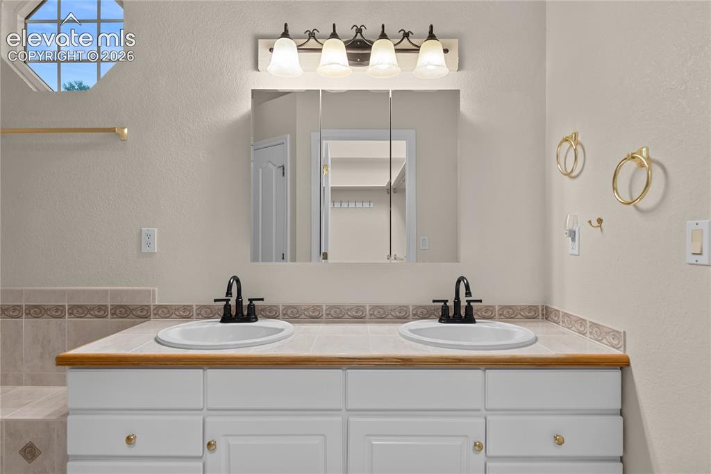 Image 25 of 41: Dual vanity featuring white cabinetry with gold-tone hardware, a light wood