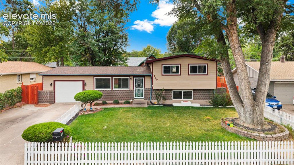 Image 1 of 36: Split-level residence featuring a white picket fence, attached single-car g
