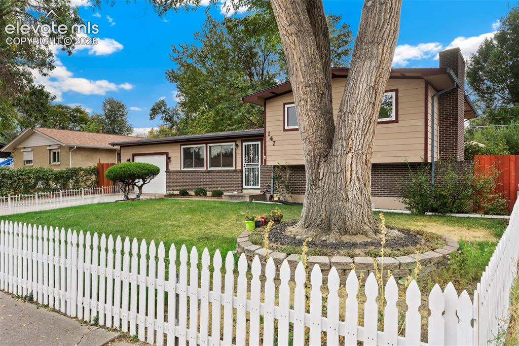 Image 10 of 36: Picket fence front yard with a mature tree, manicured lawn, and an attached