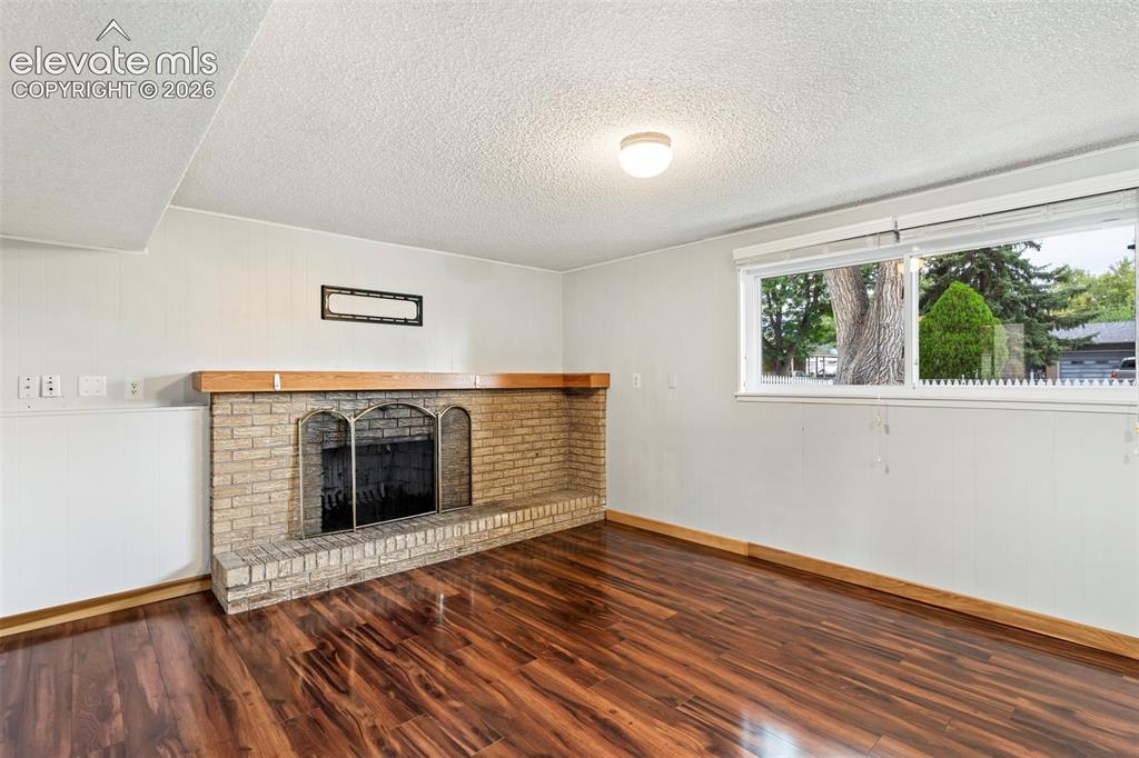 Image 21 of 36: Brick fireplace with a wood mantel, wood-finish flooring, and a large windo