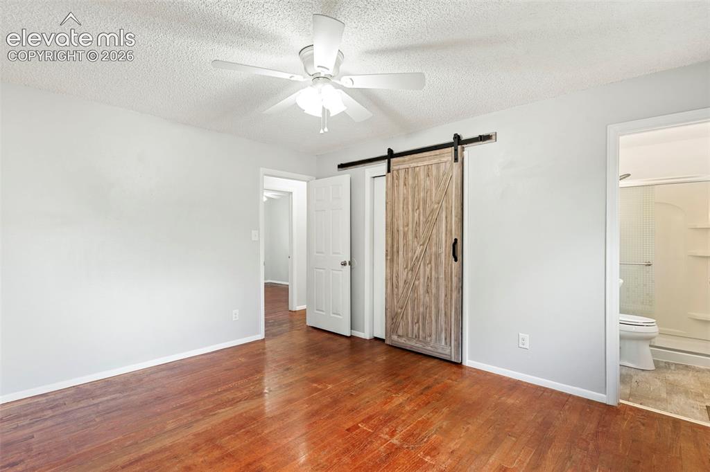 Image 23 of 36: Hardwood flooring, ceiling fan with light fixture, wood-finish barn door, a