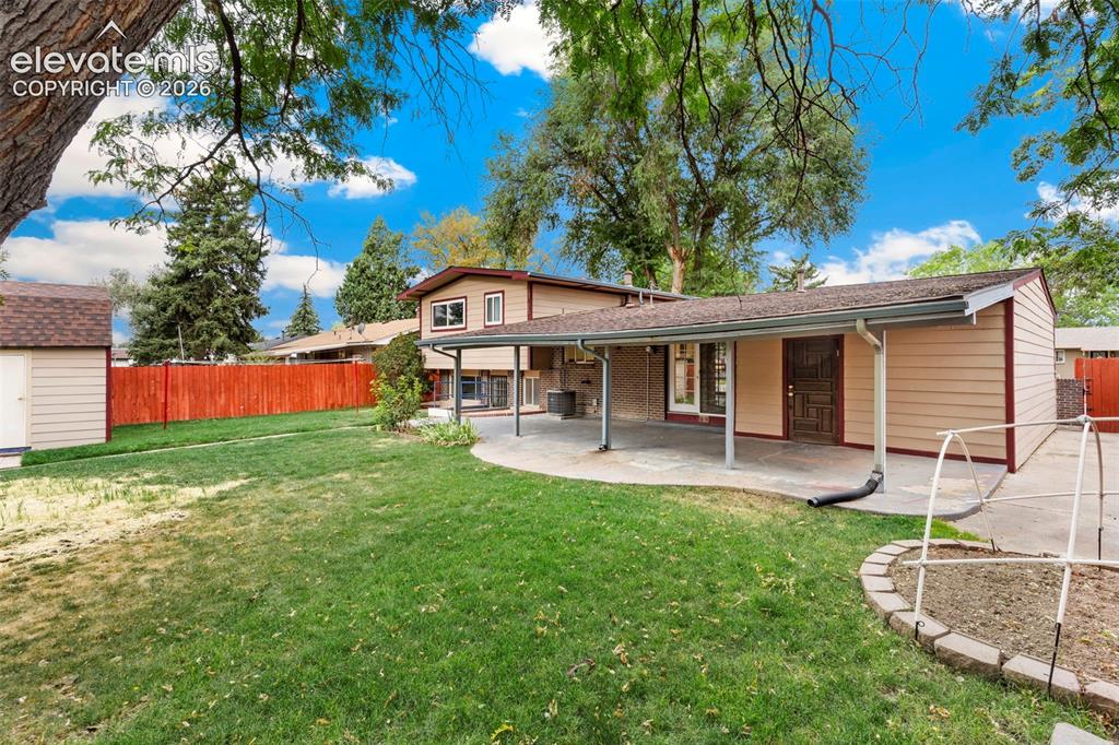 Image 34 of 36: Expansive backyard with a covered patio, manicured lawn, and mature trees