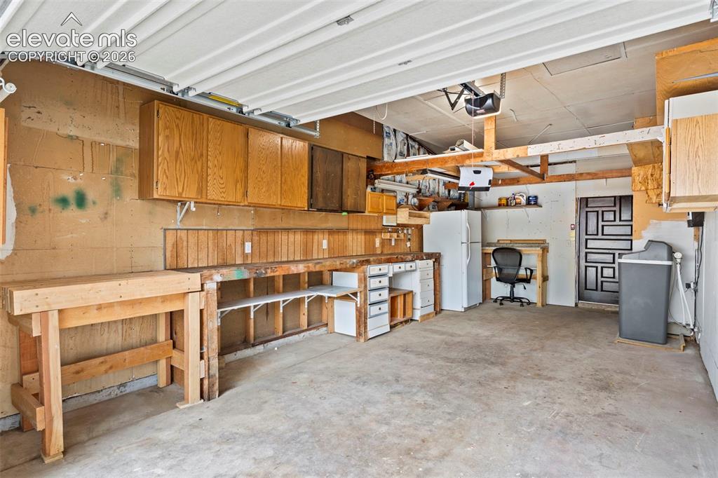 Image 36 of 36: Garage with overhead door, built-in wooden workbench, and overhead cabinetr