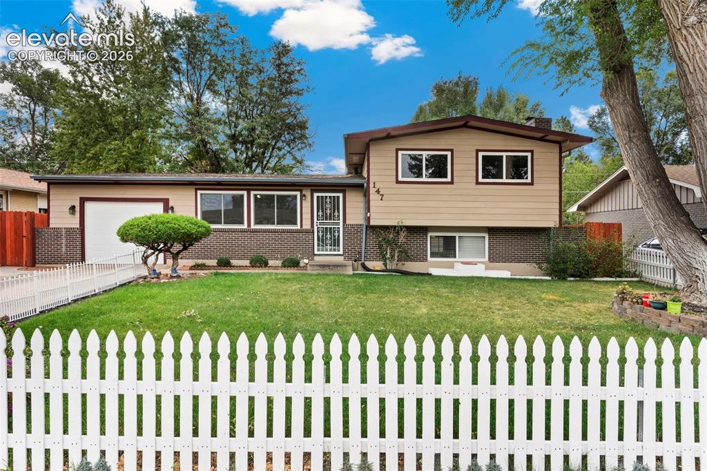 Image 9 of 36: Split-level residence featuring a white picket fence, a manicured lawn, and