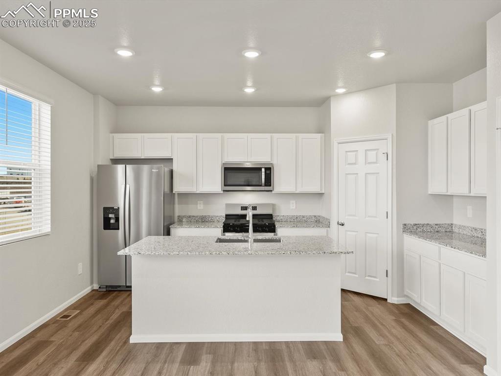 Image 2 of 26: Kitchen with white cabinets, light stone countertops, appliances with stain