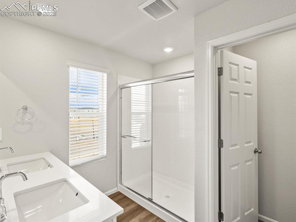 Image 22 of 26: Full bathroom with double vanity, a stall shower, wood finished floors, and