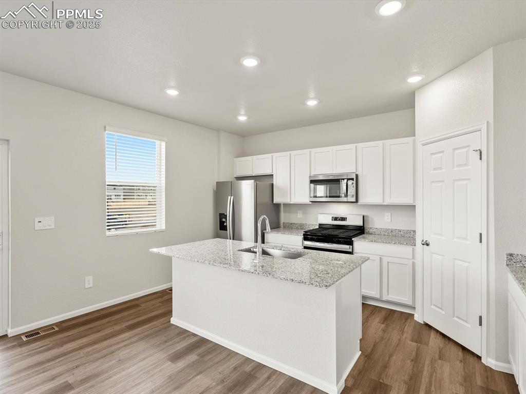 Image 3 of 26: Kitchen with light stone counters, white cabinetry, appliances with stainle
