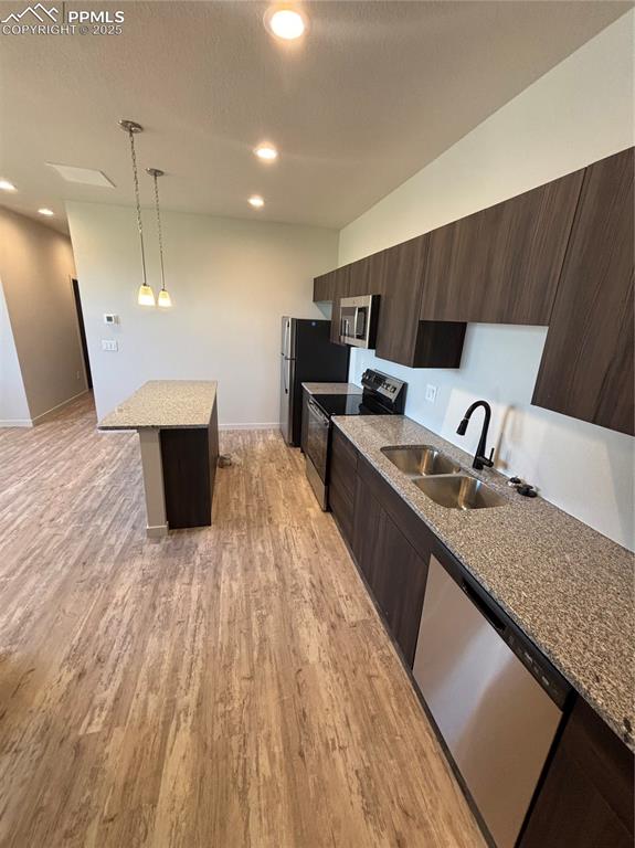 Image 8 of 13: Kitchen with dark brown cabinetry, a center island, light stone countertops