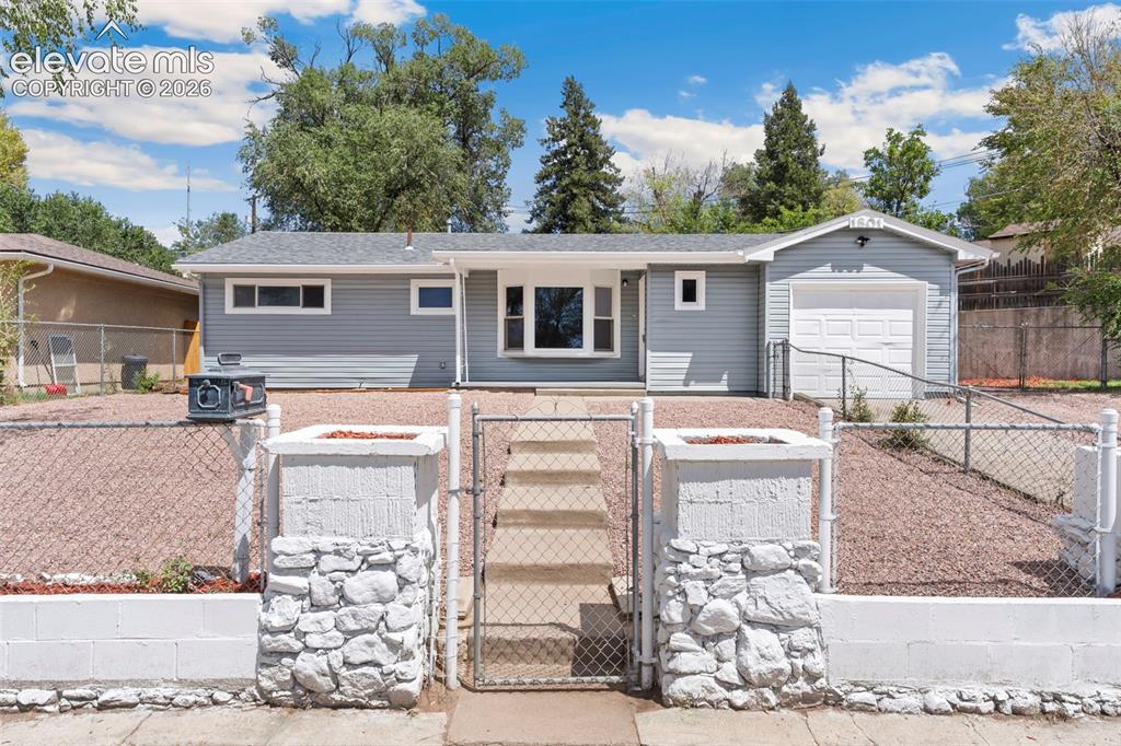 Caption: Light grey siding with white trim, attached single-car garage, white garage door, and a stone-clad e