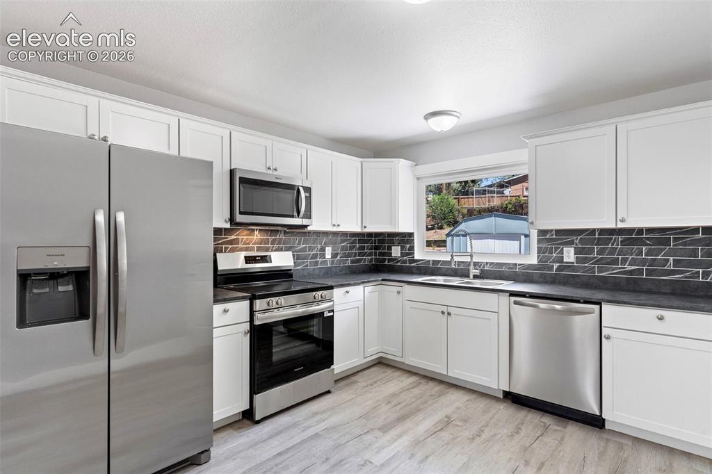 Image 16 of 33: White shaker-style cabinetry, dark countertops, full stainless steel applia