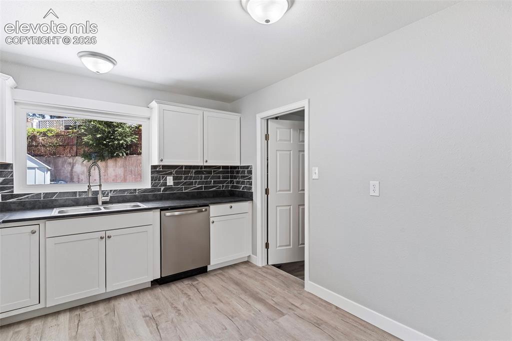 Image 18 of 33: Kitchen featuring wood-finish flooring, white cabinetry, dark countertops, 