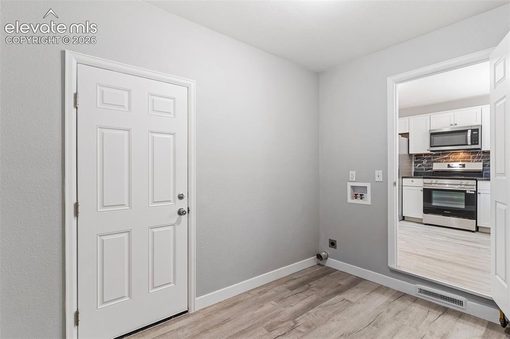 Image 19 of 33: Laundry area with wood-finish flooring, light gray walls, and white trim