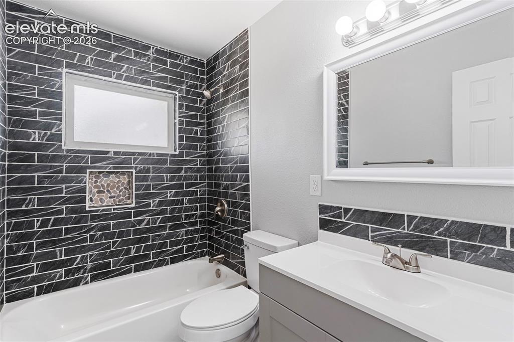 Image 26 of 33: White bathtub with a built-in shower, black subway tile surround, and a peb