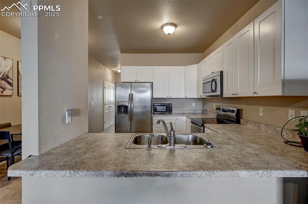 Image 5 of 29: Kitchen with appliances with stainless steel finishes, white cabinetry, lig