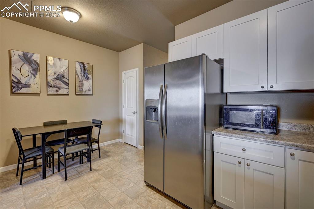 Image 7 of 29: Kitchen with stainless steel fridge, black microwave, white cabinetry, and