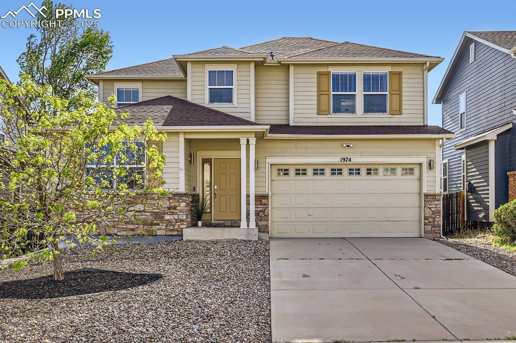 Caption: View of front of property featuring stone siding, a shingled roof, driveway, and a garage