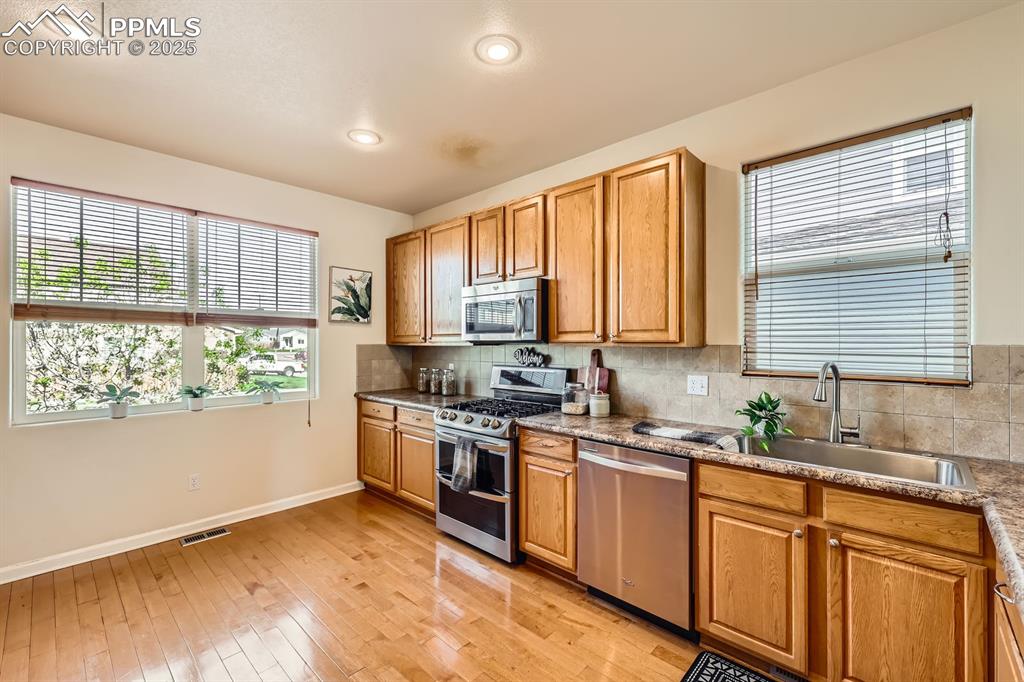 Image 10 of 39: Kitchen with stainless steel appliances, light wood-style flooring, decorat