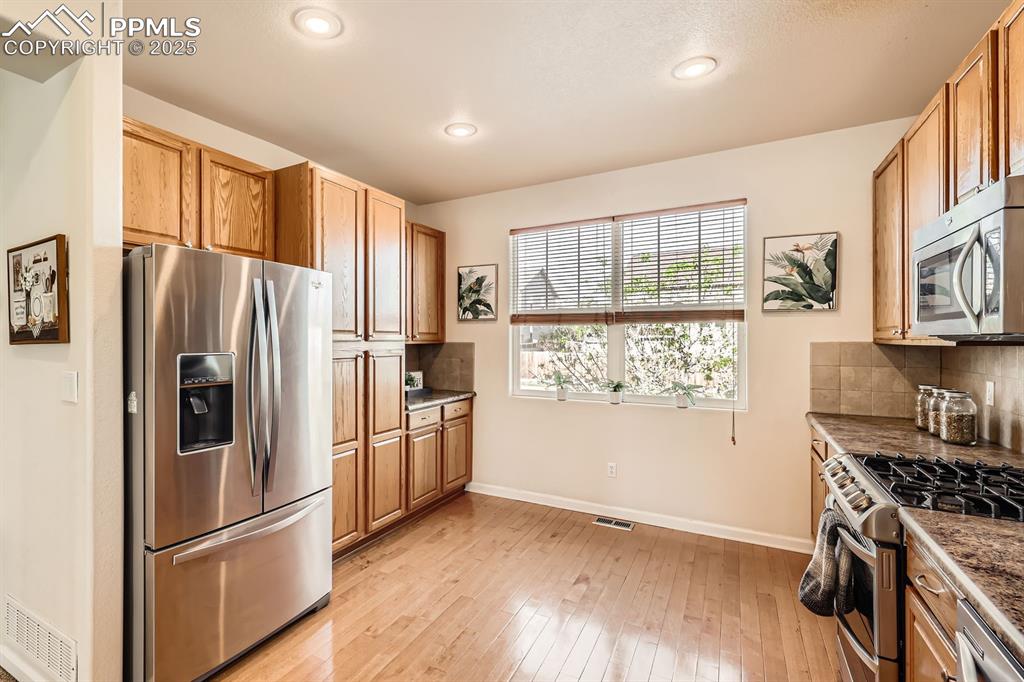 Image 13 of 39: Kitchen with stainless steel appliances, decorative backsplash, light wood 